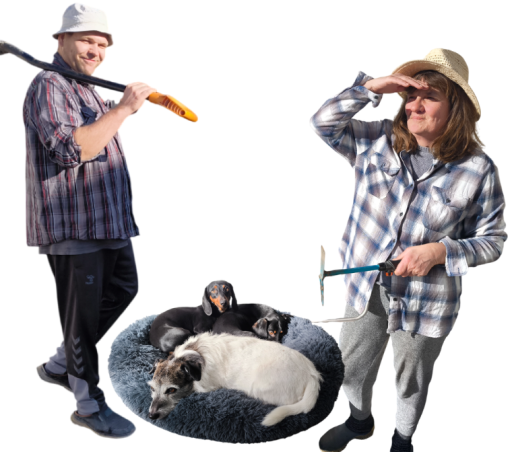 Ein Mann mit Hut und Gartenwerkzeug, eine Frau mit Strohhut, die in die Ferne blickt, und drei Hunde, die in einem flauschigen Hundebett liegen, posieren zusammen.
